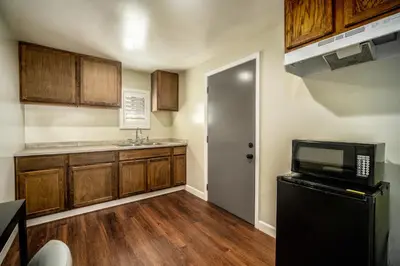 a kitchen with a black refrigerator and wooden cabinets at ERTH INN by AGA- Bell Garden in Bell Gardens