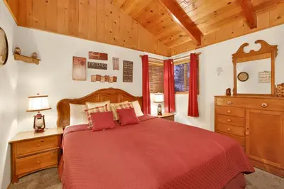 a bedroom with a red bed and a wooden ceiling at Pine Cone Cottage by Big Bear Vacations Adorable Walk To Lake Furnished Chalet in Big Bear Lake