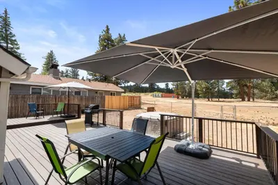 a wooden deck with a table and an umbrella at Bear Family Cabin - Stay together & play together! Foosball, billiards, hot tub, walk to lake! in Big Bear Lake