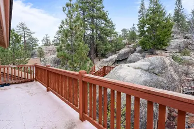 a balcony with a wooden rail and trees and rocks at Boulder Bay Chalet Lakefront - Elegantly decorated with Hot Tub and Game Room! in Big Bear Lake