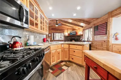 a kitchen with wooden cabinets and a stove top oven at Catalina Creekside Cabin - Log home with wood burning fireplace for an immersive mountain getaway! in Big Bear Lake