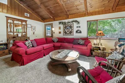 a living room with a red couch and a table at Catalina Retreat -Cozy mountain home in a tree filled neighborhood, plenty of games and a hot tub! in Big Bear Lake
