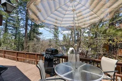 a table and chairs on a deck with an umbrella at Chalet Des Ours -Comfortable and spacious home with WIFI! Close to everything! in Big Bear Lake