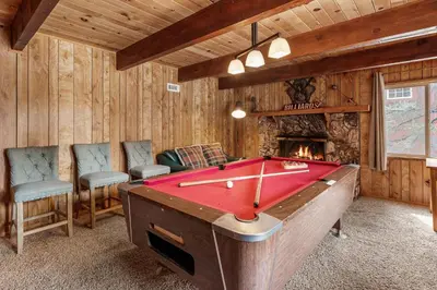 a pool table in a room with a fireplace at Forest Edge Retreat - Cozy, log cabin with a wood burning fireplace! Pool Table, Foosball and Darts! in Big Bear City