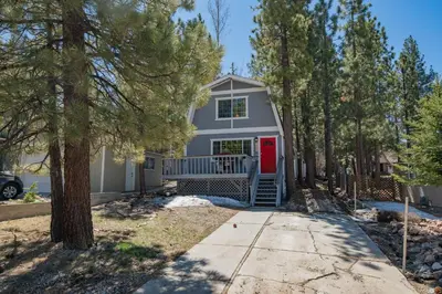 a white house with a red door and trees at Glenview Getaway - Cozy farm house! Walking distance to the lake! in Big Bear Lake