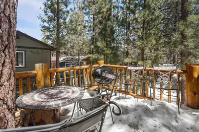 a deck with a table and chairs in the snow at Ivvy Bear Lodge - Charming log cabin with Hot tub! Short walk to Village! in Big Bear Lake