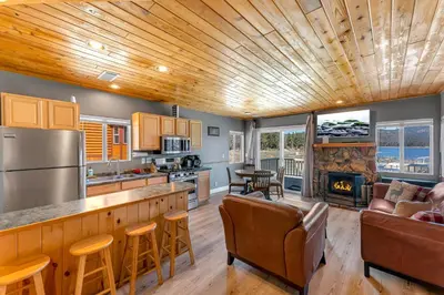a kitchen and living room with wood ceilings and a fireplace at Lakefront Oasis - Adorable lakefront cabin with a private beach! in Big Bear Lake