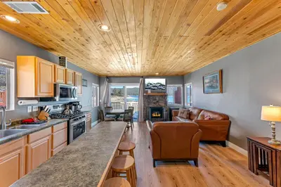a kitchen and living room with a wooden ceiling at Lakefront Oasis - Adorable lakefront cabin with a private beach! in Big Bear Lake