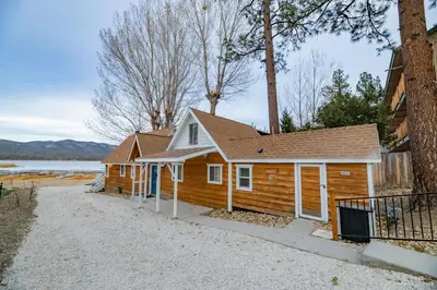 a log cabin with a lake in the background at Lakefront Oasis - Adorable lakefront cabin with a private beach! in Big Bear Lake