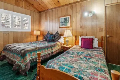 two beds in a room with wooden walls at Snowridge - Charming classic cabin with a wood burning fireplace and WiFI! in Big Bear City