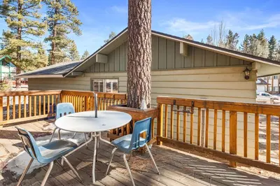 a table and chairs on a deck with a tree at Snowridge - Charming classic cabin with a wood burning fireplace and WiFI! in Big Bear City