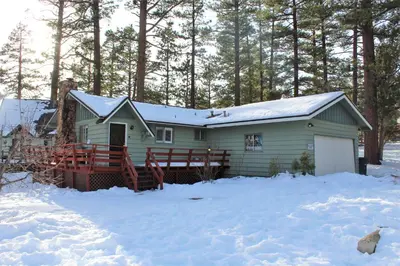 a green house in the snow with trees at Snowridge - Charming classic cabin with a wood burning fireplace and WiFI! in Big Bear City