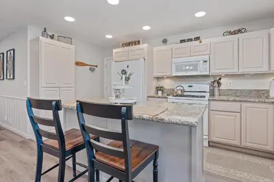 a kitchen with white cabinets and two chairs at a counter at Serenity Knoll - Comfortable, spacious single-level cabin! Newly remodeled! Hot Tub and Pool Table! in Big Bear Lake