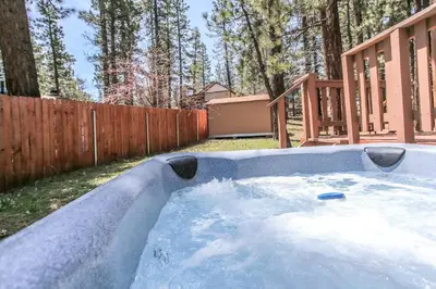 a hot tub in a backyard with a wooden fence at Rincon Cabin - Close to the lake with a huge fenced in yard! Hot tub and deck with barbecue! in Big Bear Lake