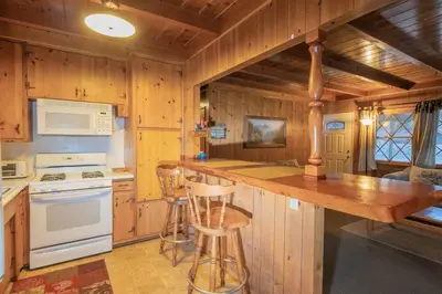 a kitchen with wooden walls and a counter with stools at Sauer Suite - Cozy, rustic cabin walking distance to Holloway's Marina with peek-a-boo lake views! in Big Bear Lake