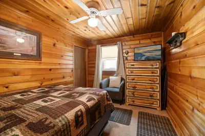 a bedroom with a bed and a chair in a room at Pine Forest Cabin - Adorable vintage cabin with a cozy wood burning fireplace and foosball table! in Big Bear Lake