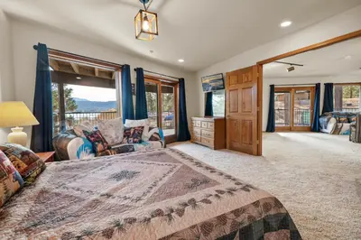 a bedroom with a large bed and a living room at North Shore Lakefront - Spacious Lakefront with Hot Tub, & Game Room in Fawnskin