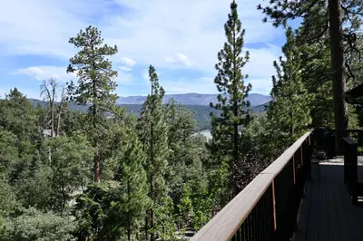 a balcony with a view of trees and mountains at Nightcap Lodge- HOT TUB WITH BREATHTAKING MOUNTAIN VIEWS! in Fawnskin