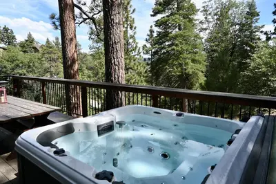 a jacuzzi tub on a deck with trees at Nightcap Lodge- HOT TUB WITH BREATHTAKING MOUNTAIN VIEWS! in Fawnskin