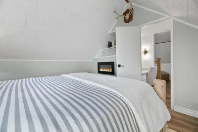 a white bedroom with a bed and a fireplace at Boulder Bay Bungalow - Updated mountain retreat with hot tub, game table, and sauna! in Big Bear Lake