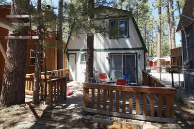 a house with a porch and a deck with chairs at Bear 'n Tree - Cozy cabin near the Village in Big Bear Lake