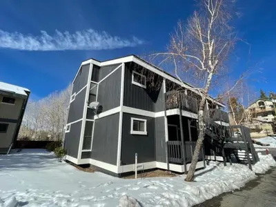 a gray house in the snow with a tree at Boulder Bay Chalet Condo - Mountain charm condo with lake view and WIFI! in Big Bear Lake