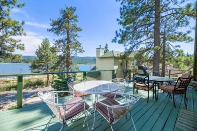 a deck with tables and chairs and a view of the water at Moonlight Shores Lakefront - Lakefront home with hot tub! in Fawnskin