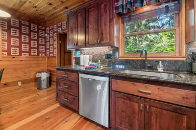 a kitchen with wooden cabinets and a sink and a window at Stillwater Cove Lakefront - Breathtaking views, charming vintage cabin, woodsy interior! Boat Dock! in Big Bear Lake