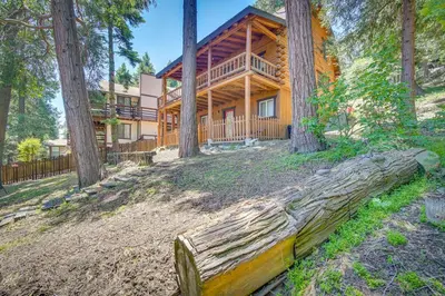 a large log cabin in the woods with a fence and trees at Crestline Area Vacation Rental Cabin with Decks! in Crestline