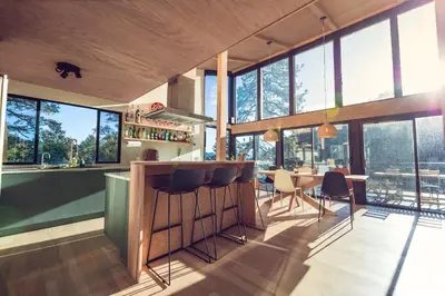 a kitchen with a bar and a dining room with windows at Spectacular Designer Treehouse with Mountain Views in Pine Mountain Club