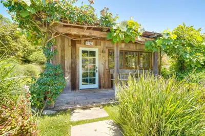 a small wooden building with a door in a garden at Farmhouse-Chic Carpinteria Cottage with Pool Access in Carpinteria
