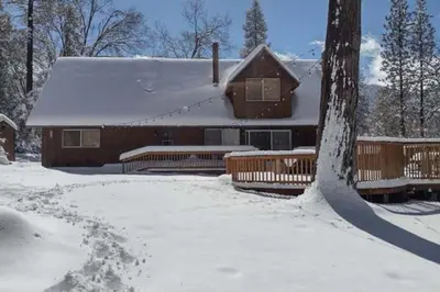 a house is covered in snow with a tree at Sequoia Retreat- Spacious Cabin, Hot tub, & Sundeck in Ponderosa