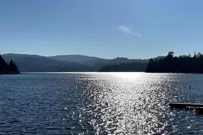 a large lake with the sun reflecting on the water at NEW & Luxurious House, hot tub & amazing views in Lake Arrowhead