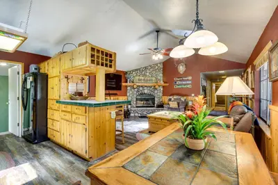 a kitchen with wooden cabinets and a living room at Central Big Bear Lake Retreat with Private Hot Tub! in Big Bear Lake