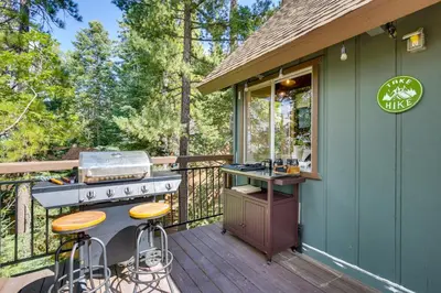 a outdoor kitchen with a grill and stools on a deck at Cozy and Chic Lake Arrowhead Cabin with Deck! in Lake Arrowhead