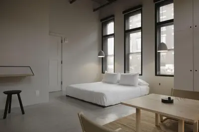 a bedroom with a bed and a table and windows at kodō hotel - Heart of LA Arts District in Los Angeles