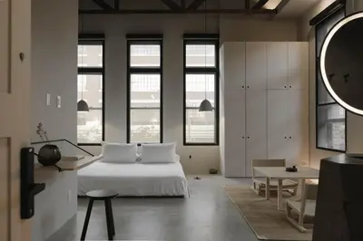 a bedroom with a bed and a table and some windows at kodō hotel - Heart of LA Arts District in Los Angeles