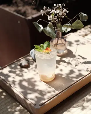 a drink sitting on a table with a vase of flowers at kodō hotel - Heart of LA Arts District in Los Angeles