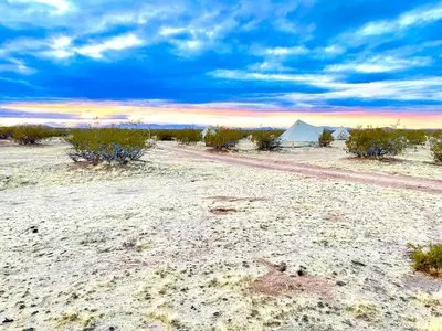 a dirt road in the desert with tents in the distance at Beysicair Tents & Campground in California City