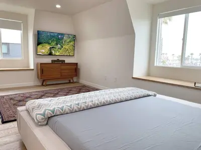 a bedroom with a bed and a dresser and windows at Oceanfront Penthouse On Sand - Epic Views/Sunsets! in Huntington Beach
