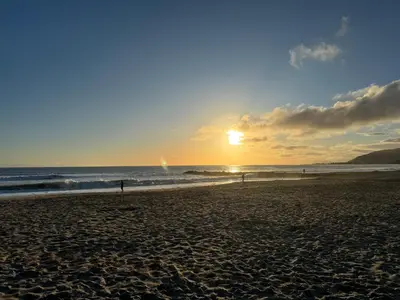a sunset on a beach with people walking on the sand at The Shores Inn in Ventura