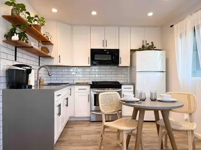 a kitchen with white cabinets and a table with chairs at The Cozy Oasis - A Renovated and Modern Studio near LAX + SoFi + Beaches + Freeway in Lawndale