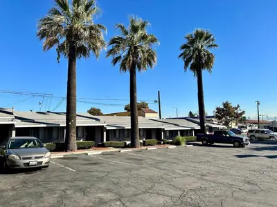 a parking lot with palm trees in front of a motel at Pala Motel in Pomona