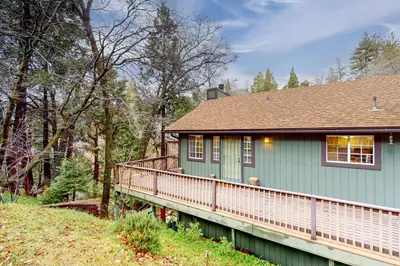 a green house with a wooden balcony in the woods at Creekside Cabin in Crestline