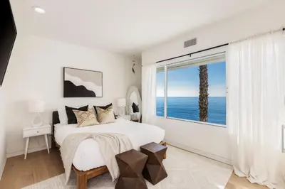 a white bedroom with a bed and a large window at Malibu Breeze - hot tub, ocean view, steps to beach in Malibu