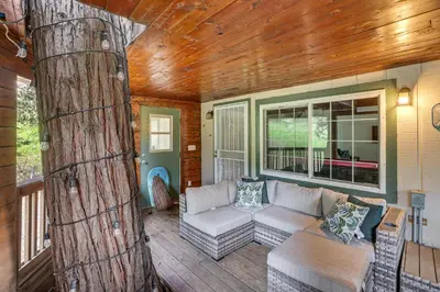 a living room with a couch and a tree at Crestline Home with Private Hot Tub Steps to Lake! in Crestline