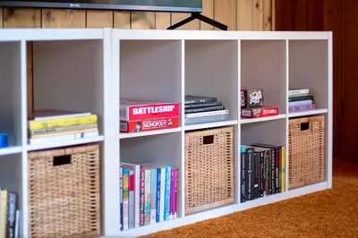 a white book shelf filled with books and baskets at Pet & Kid Friendly Cozy Cabin, BBQ, Firepit, Outdoor Dining, Forest Views in Lake Arrowhead