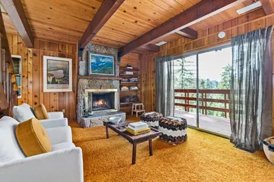 a living room with a fireplace and a large window at Pet & Kid Friendly Cozy Cabin, BBQ, Firepit, Outdoor Dining, Forest Views in Lake Arrowhead