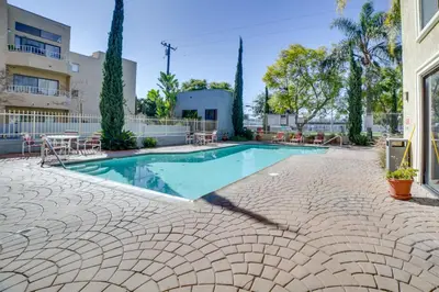 a swimming pool with tables and chairs next to a building at 1 Mi to the Ocean Long Beach Condo with Pool Access in Long Beach