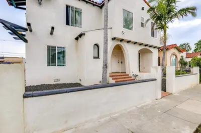 a white house with a gate and a palm tree at 9 Mi to Dodger Stadium! East LA Studio with Patio in East Los Angeles